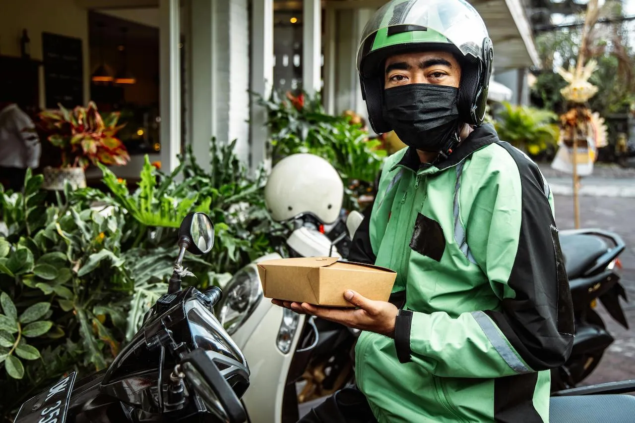 A Man In Black and Green Jacket Holding a Box of Food.