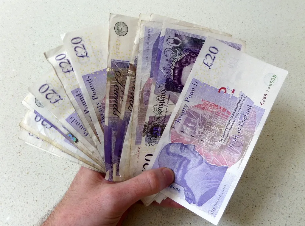A hand holding a stack of british pound banknotes.