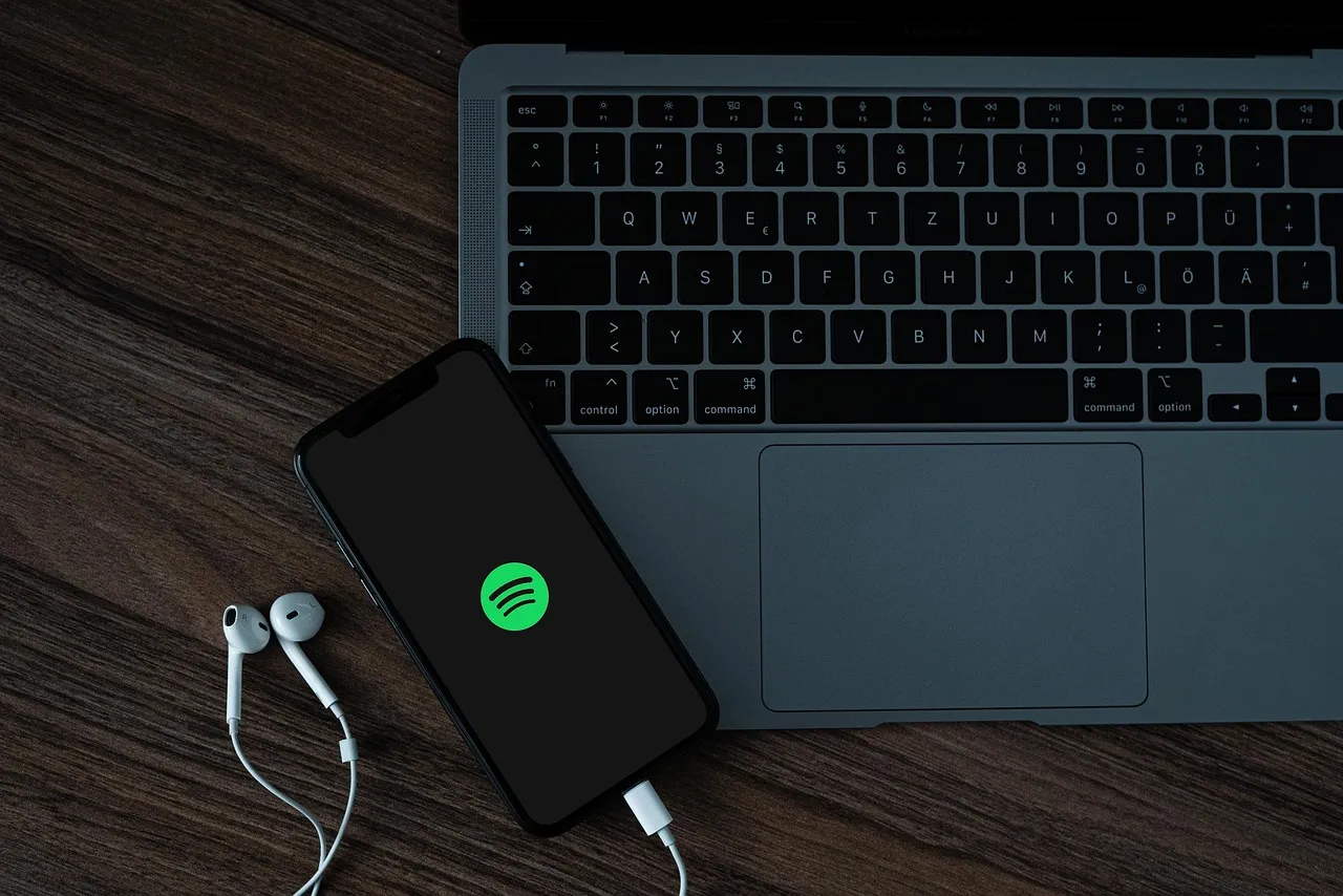 A mobile phone with the Spotify logo, near a MacBook Pro.