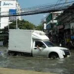 A pickup truck and a motorcycle driving through a flooded street in Bangkok