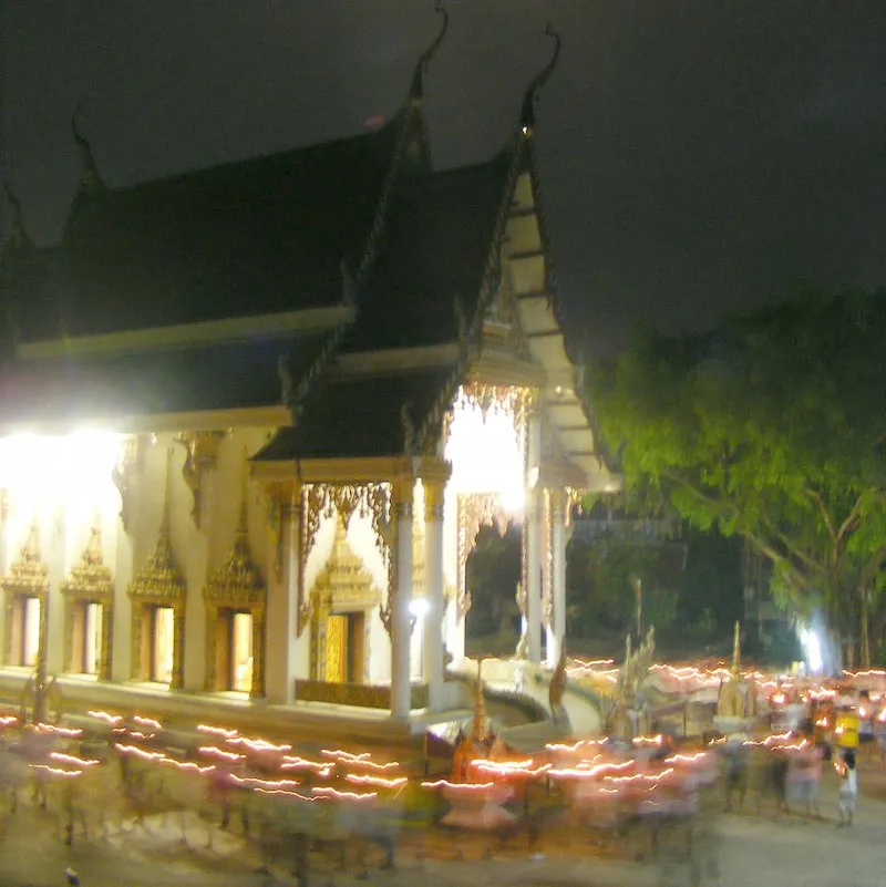 Walk with lighted candles in hand around a temple on Asalha Puja day