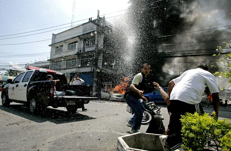 Thai policemen assist an injured person after a grenade bomb exploded outside a police station in Pattani