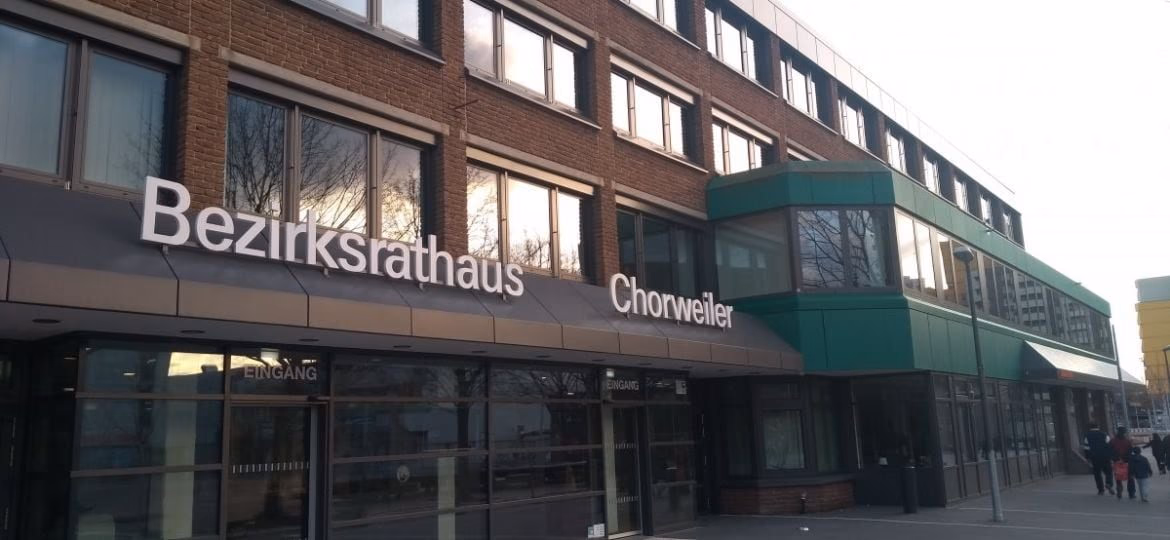 Bezirksamt Lindweiler in modernem Gebäude mit transparenten Glasfassaden und Hinweisschildern, Gebäudefront mit Fokus auf offizielle Verwaltungsstätte in Lindweiler.