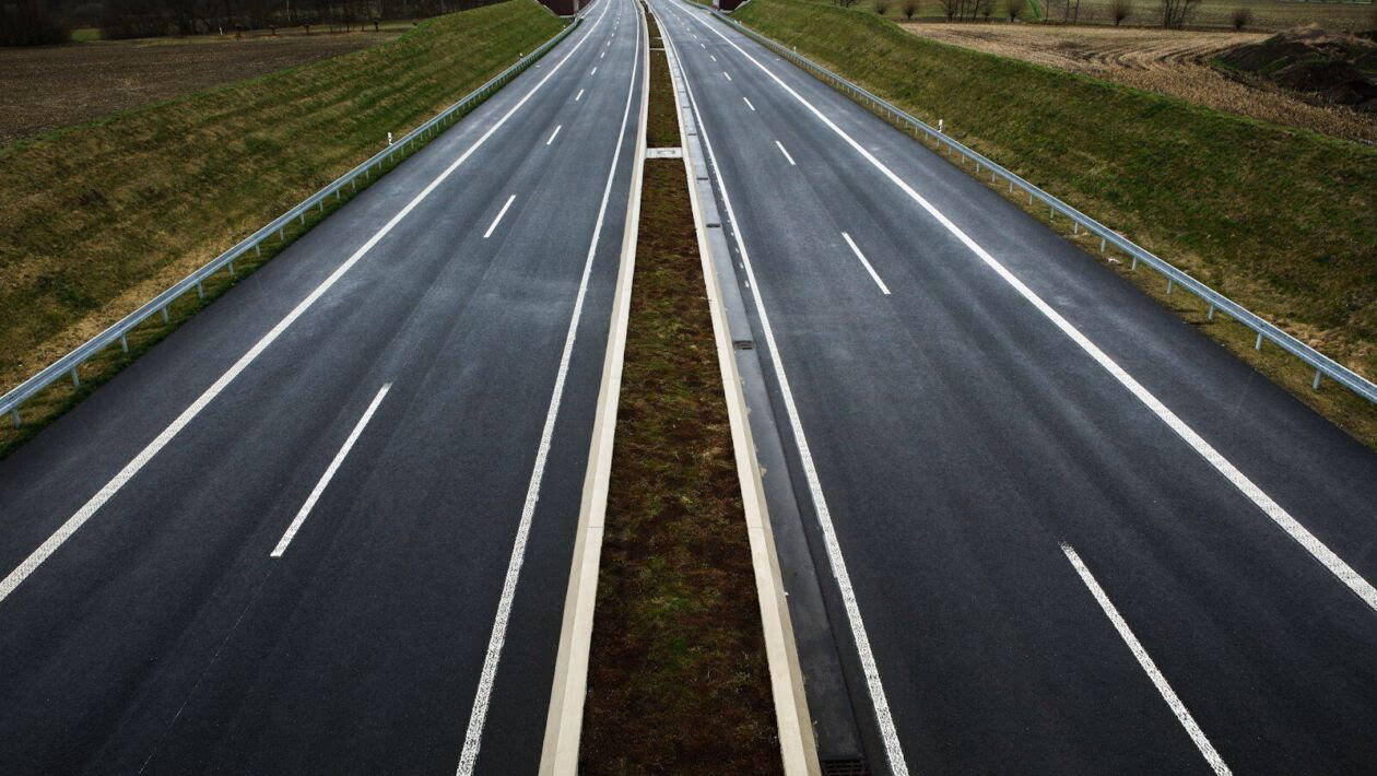 Leere Autobahn in ländlicher Gegend, asphaltierte Straßen mit Markierungen, grüne Nebenflächen, Wolkenverhangener Himmel, modernes Straßendesign, ruhige ländliche Umgebung, Lindweiler, Deutschland.