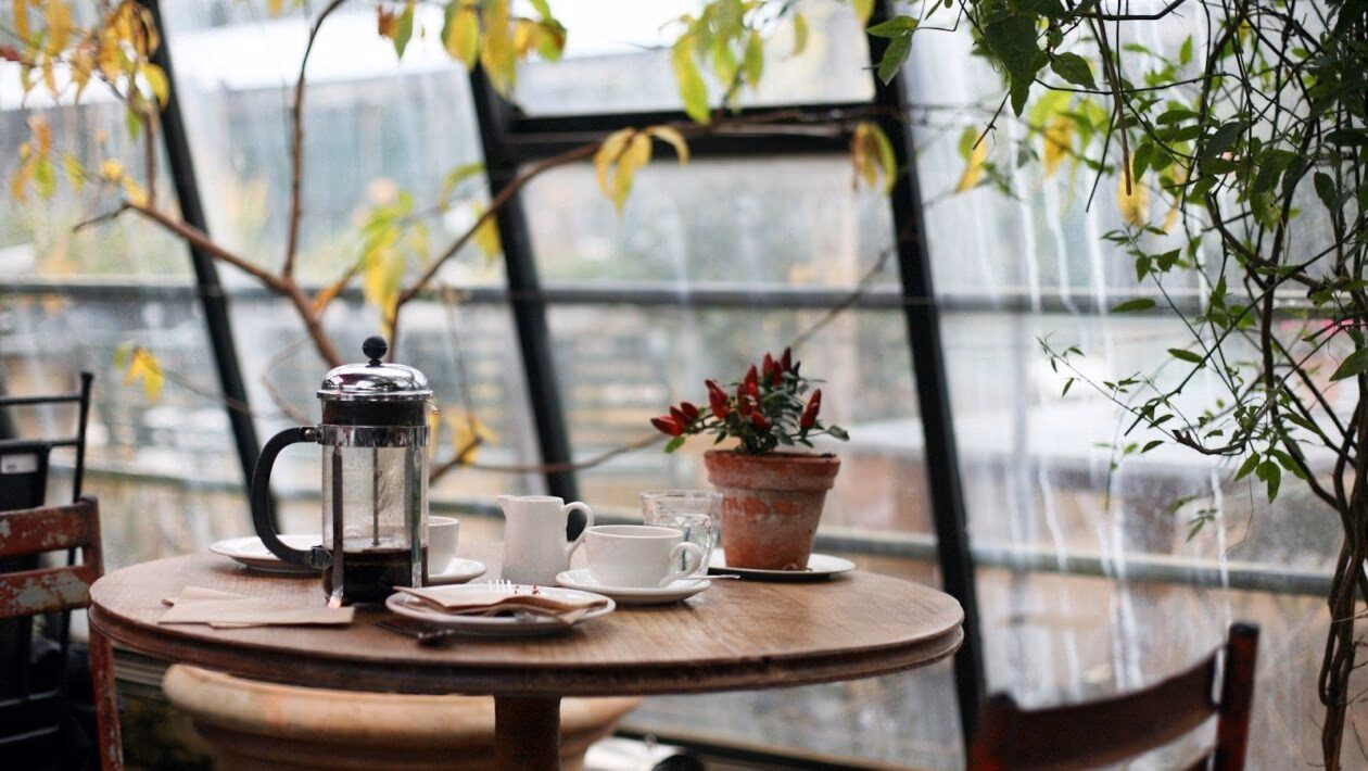 round brown wooden table with french press on top with white ceramic teacup beside